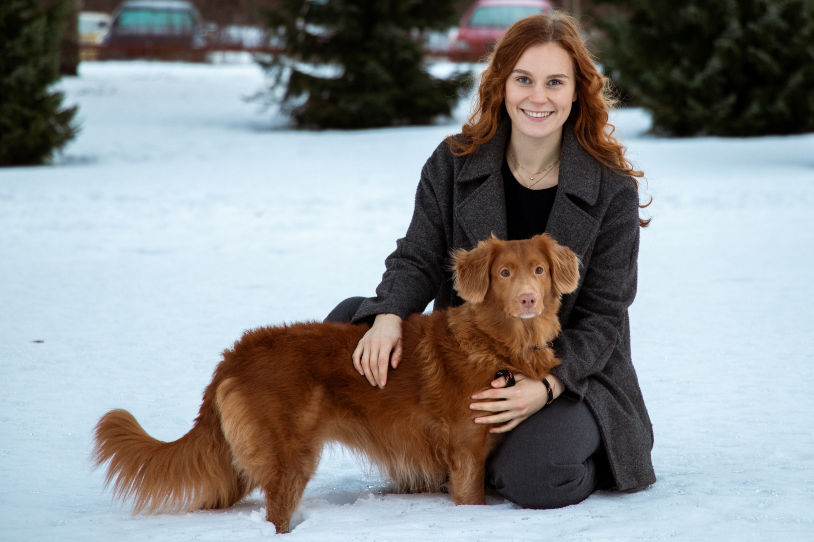 Hymyilevä Marianna punaruskean novascotiannoutajan kanssa ulkona lumihangessa. Koira seisoo kyykistyneen Mariannan edessä, ja molemmat katsovat kameraan.