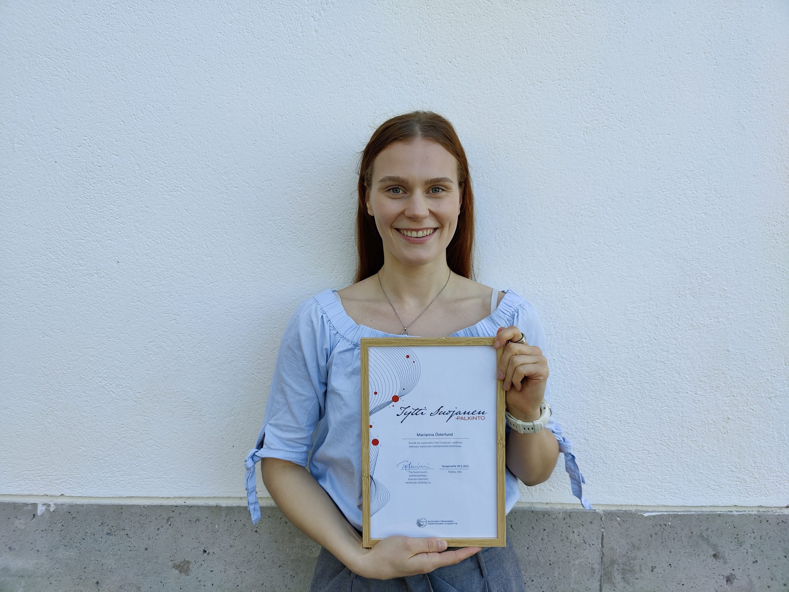 Marianna hymyilee ja pitää Tytti Suojanen -palkinnon kunniakirjaa kädessään.