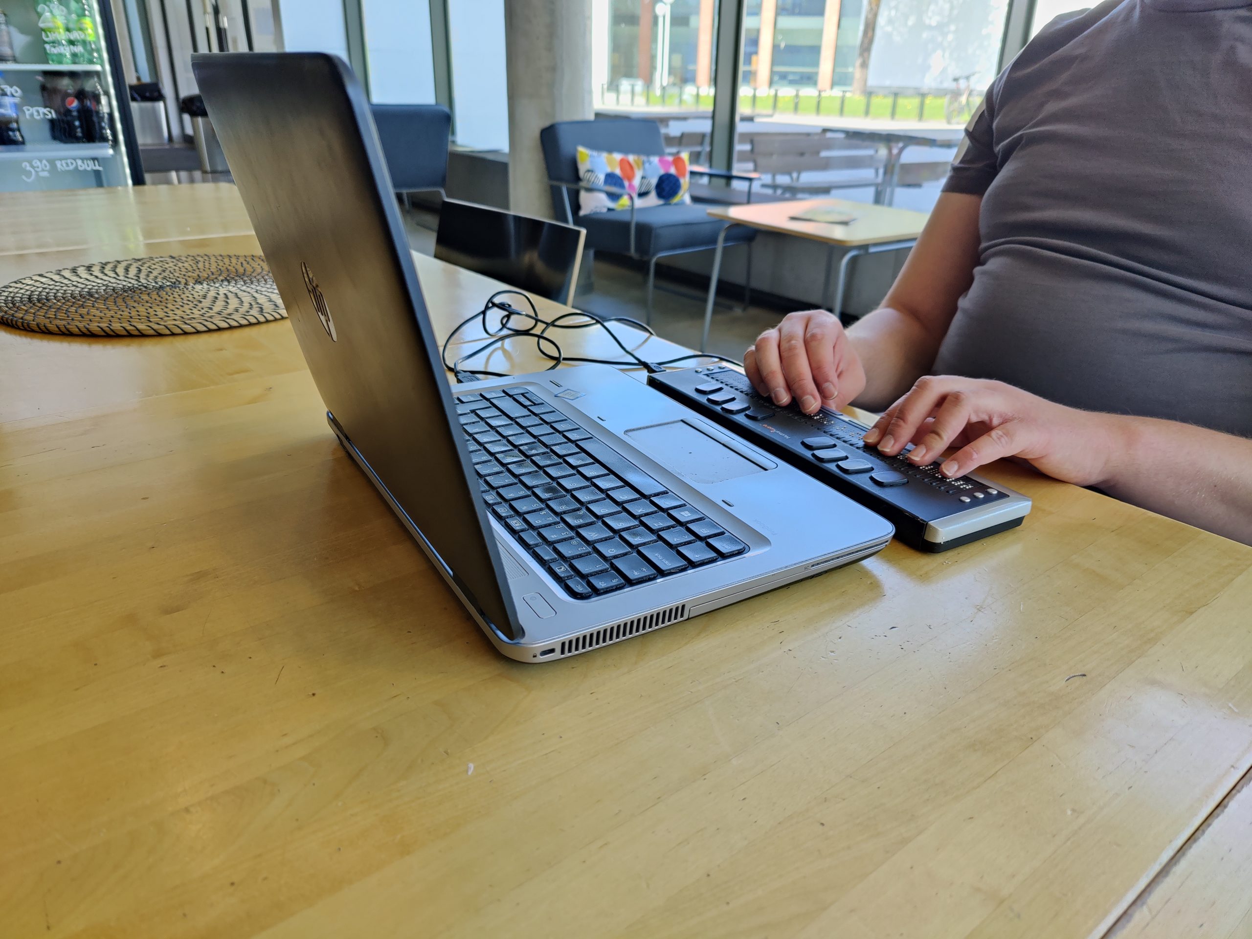 Lähikuva pistenäyttöä käyttävistä käsistä, pistenäyttö on kannettavan tietokoneen edessä pöydällä.