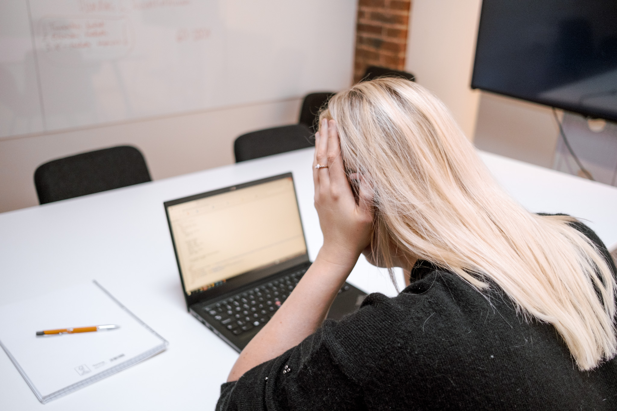 Vaaleatukkainen nainen nojaa käteensä katsoessaan edessään olevaa kannettavaa tietokonetta.